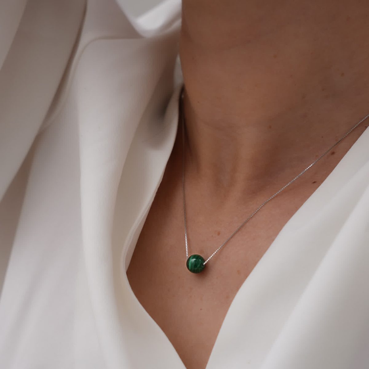 Dainty malachite bead necklace worn close to skin with simple gold-toned styling.