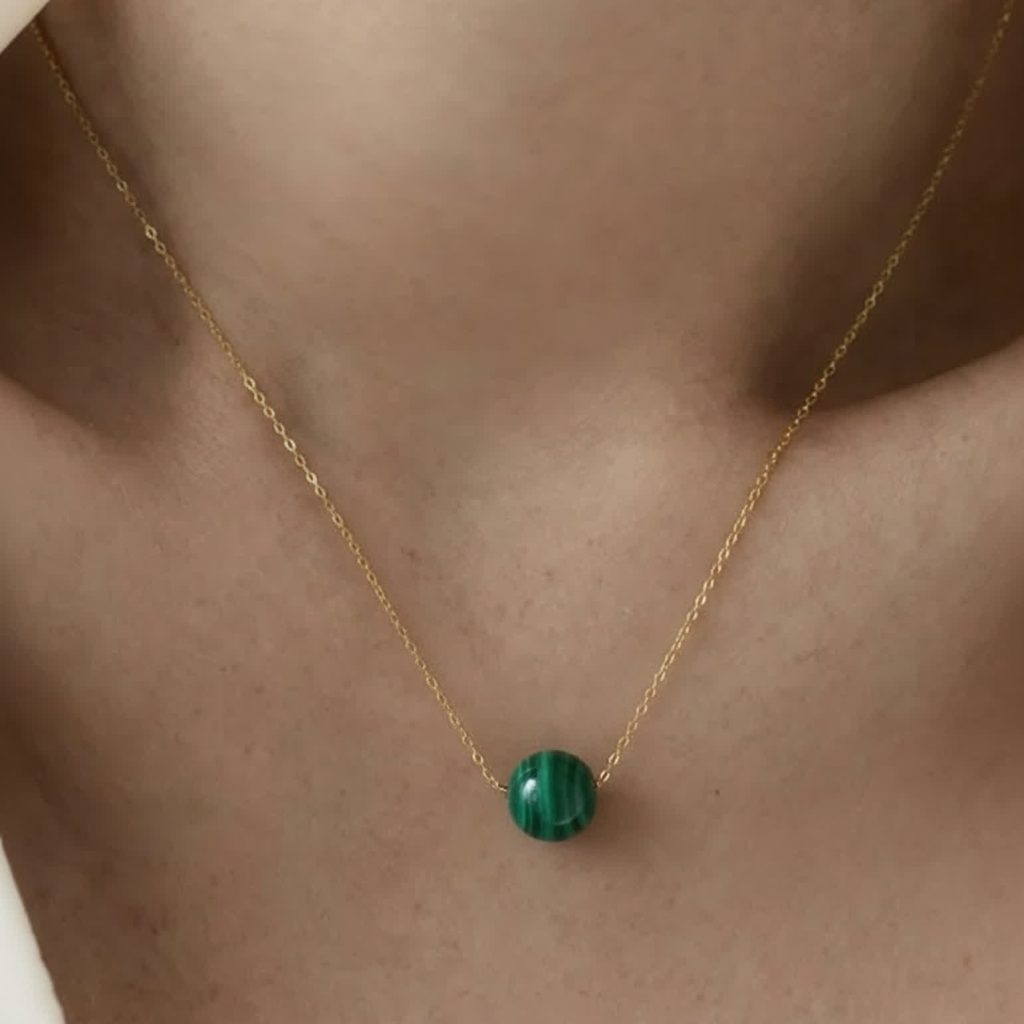 Dainty malachite bead necklace worn close to skin with simple gold-toned styling.