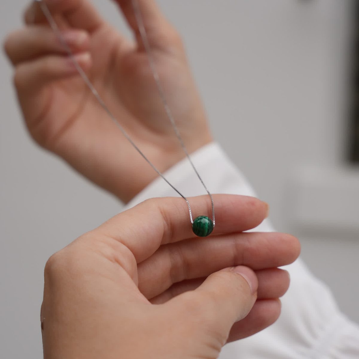 Hand adjusting delicate malachite bead necklace highlighting petite pendant scale.