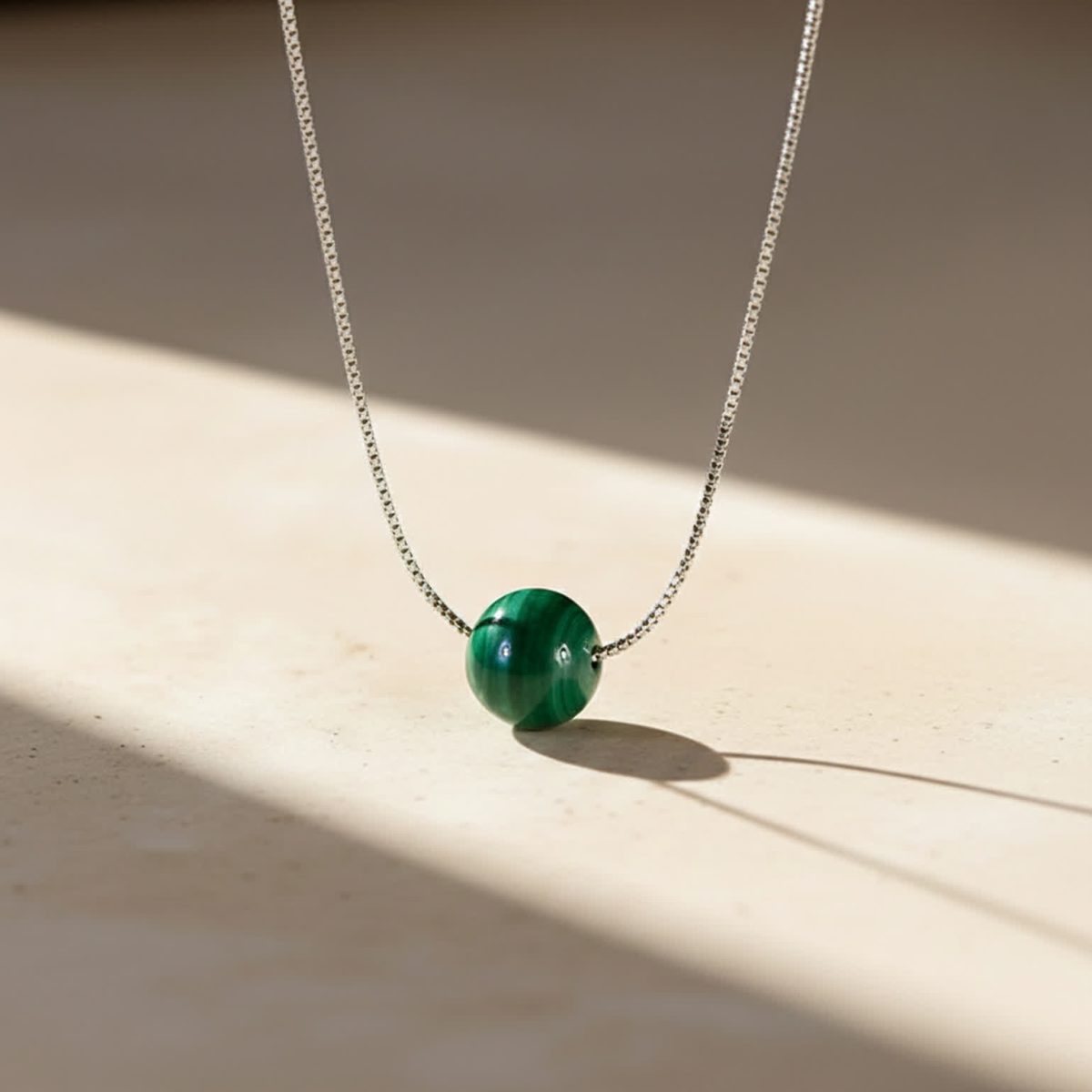 Minimalist malachite pendant necklace resting flat with smooth silver chain detail visible.