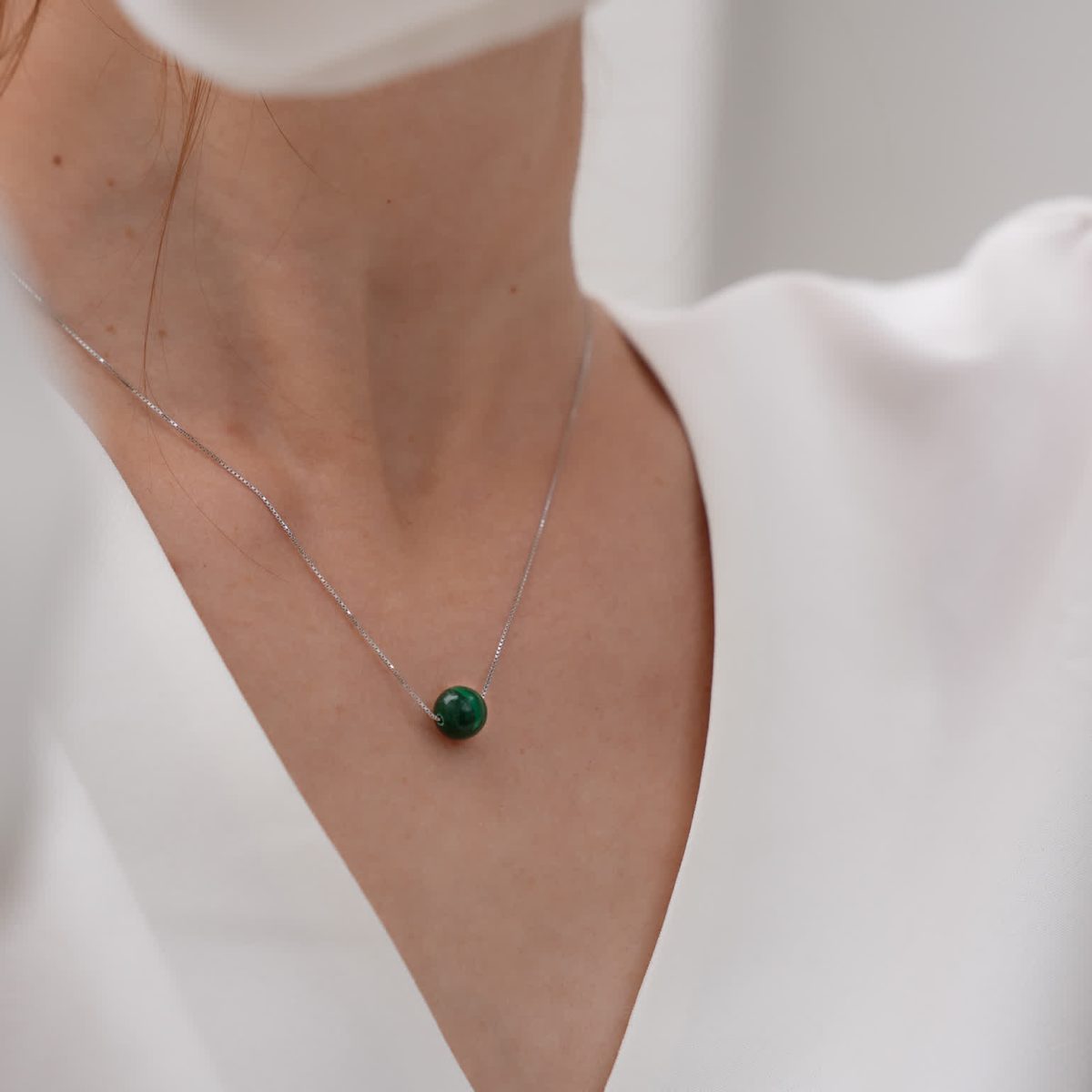 Model wearing small green malachite bead necklace layered over white blouse neckline.