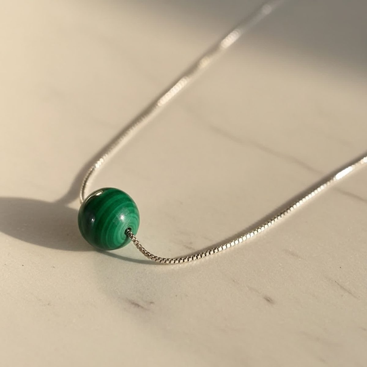 Close view of 8mm green malachite bead held between fingers showing polished finish.