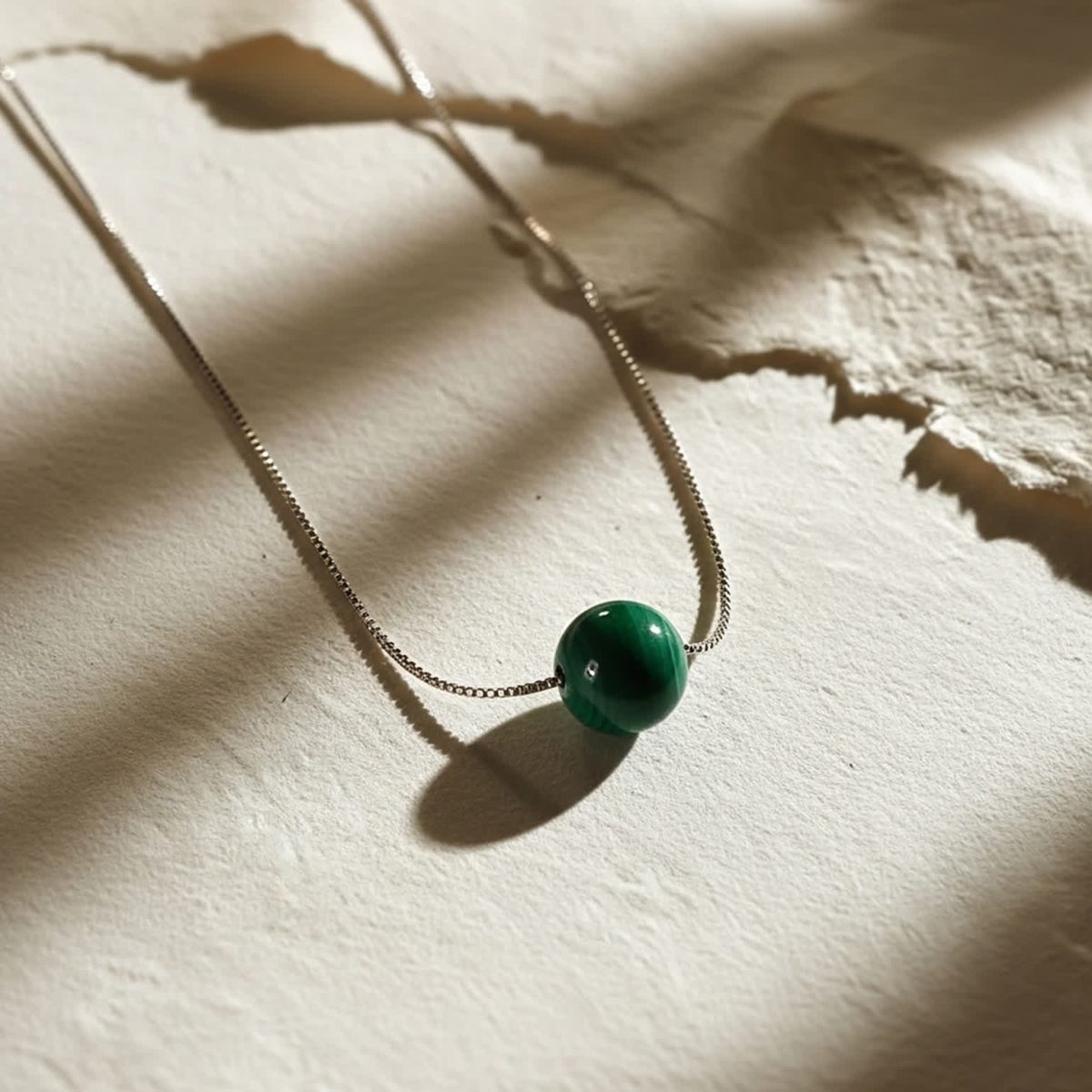 Natural malachite bead necklace displayed beside stone surface with soft shadows.