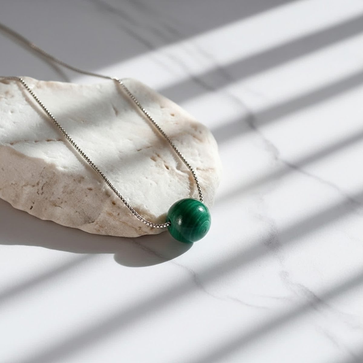 Polished green malachite bead necklace on fine sterling silver chain against neutral background.