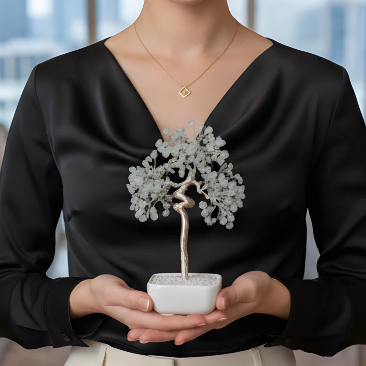 Woman holding an aquamarine crystal tree bonsai with blue gemstone chips in a white ceramic bowl