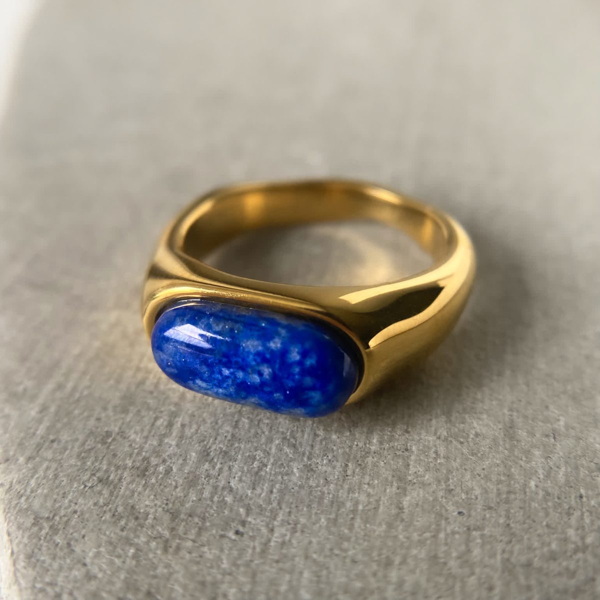 Polished lapis lazuli ring set in smooth 18K gold plated band on neutral background.