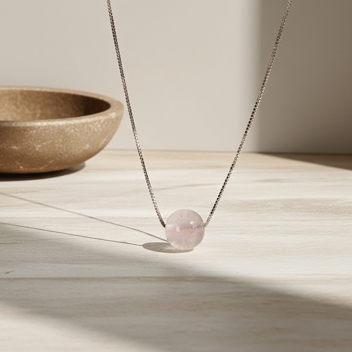 Hand holding natural rose quartz pendant on silver chain