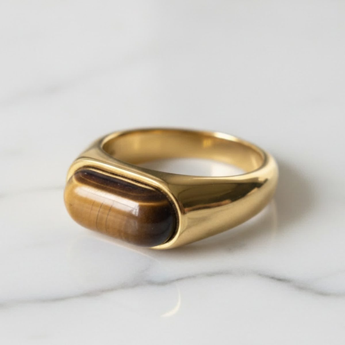 Polished tiger eye ring in 18K gold plated band displayed on marble surface.