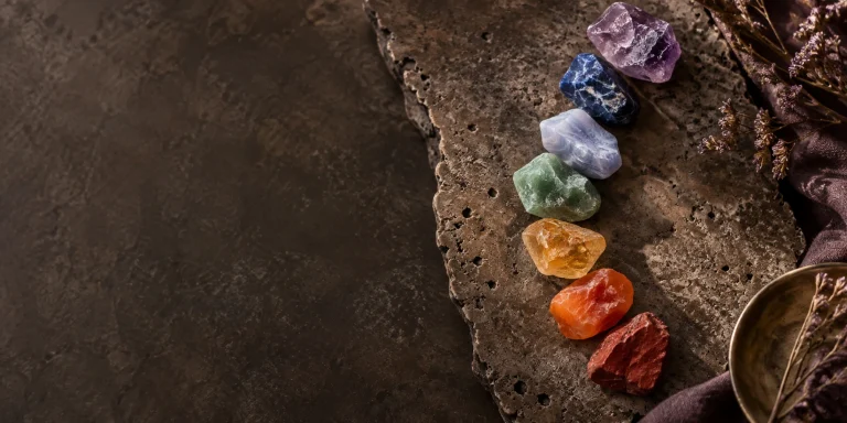 Seven natural chakra stones from red jasper to amethyst arranged on travertine