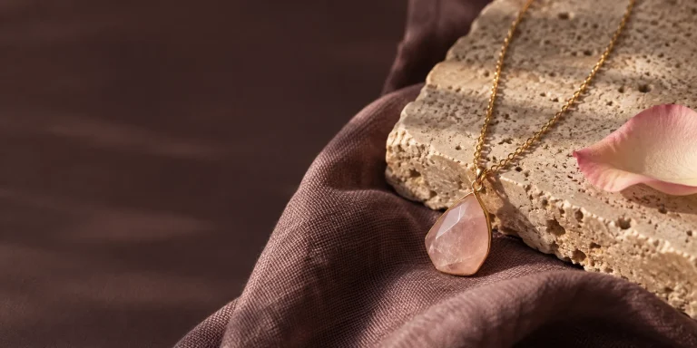 Gold necklace with a pale rose quartz pendant on travertine